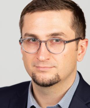 Erick Amick, a male-presenting person who smiles towards the camera against a light-gray background.