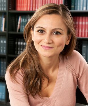Leyla Ismayilova, a female-presenting person, smiles towards the camera in a library.